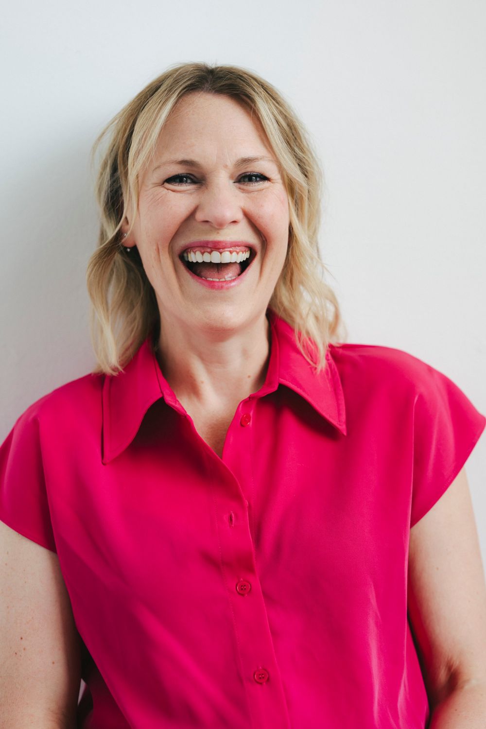 Kate Maddison-Greenwell laughing, in a pink shirt against a white wall