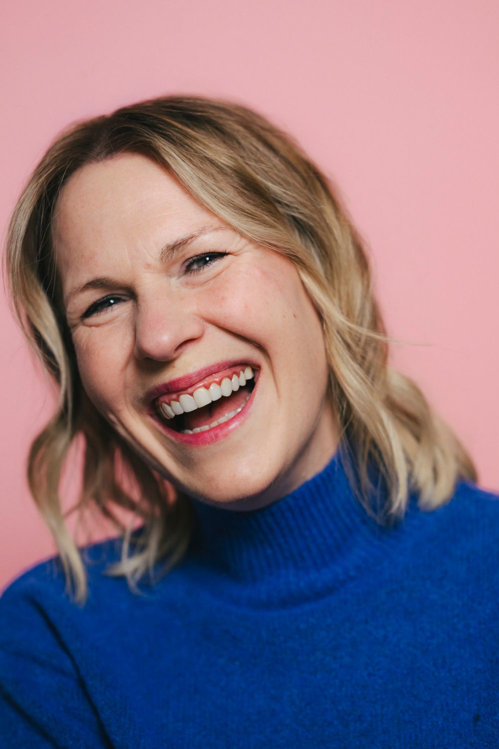 Kate laughing against a pink backdrop, wearing a blue jumper
